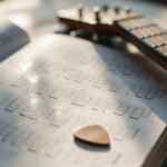 Manche de guitare et médiator posés sur un livre de partitions ouvert